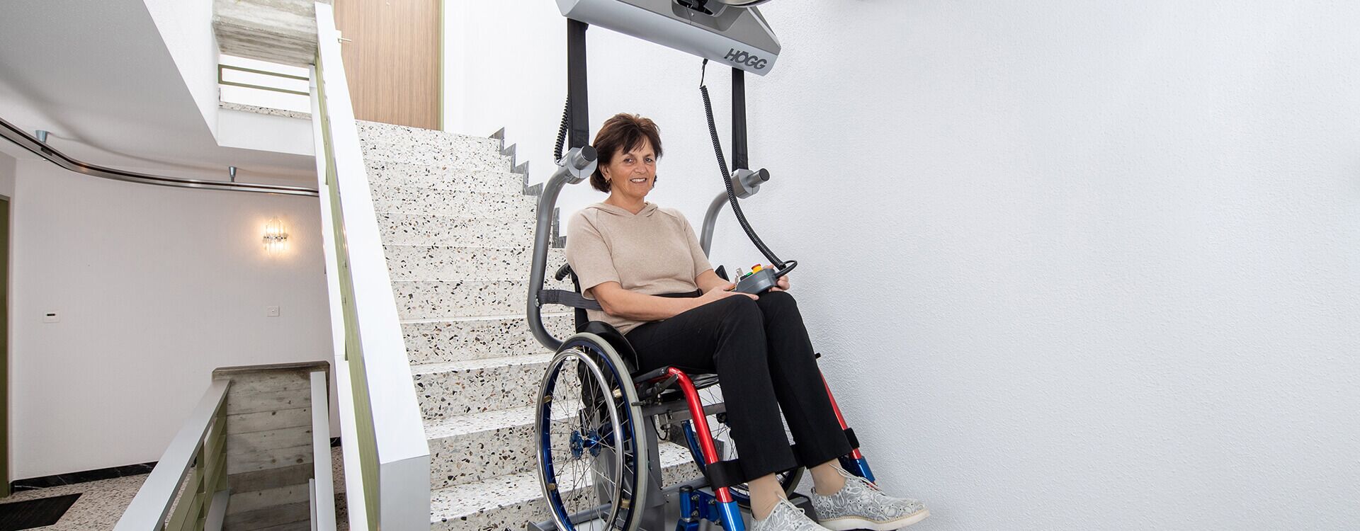 Deckengeführter Rollstuhllift mit eingehängtem Rollstuhl und Person - Högg